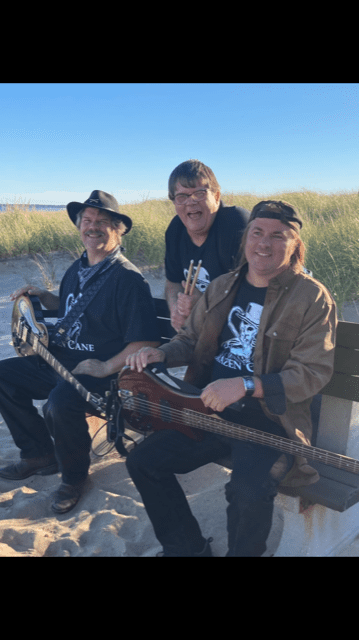Three men are sitting on a bench with guitars.