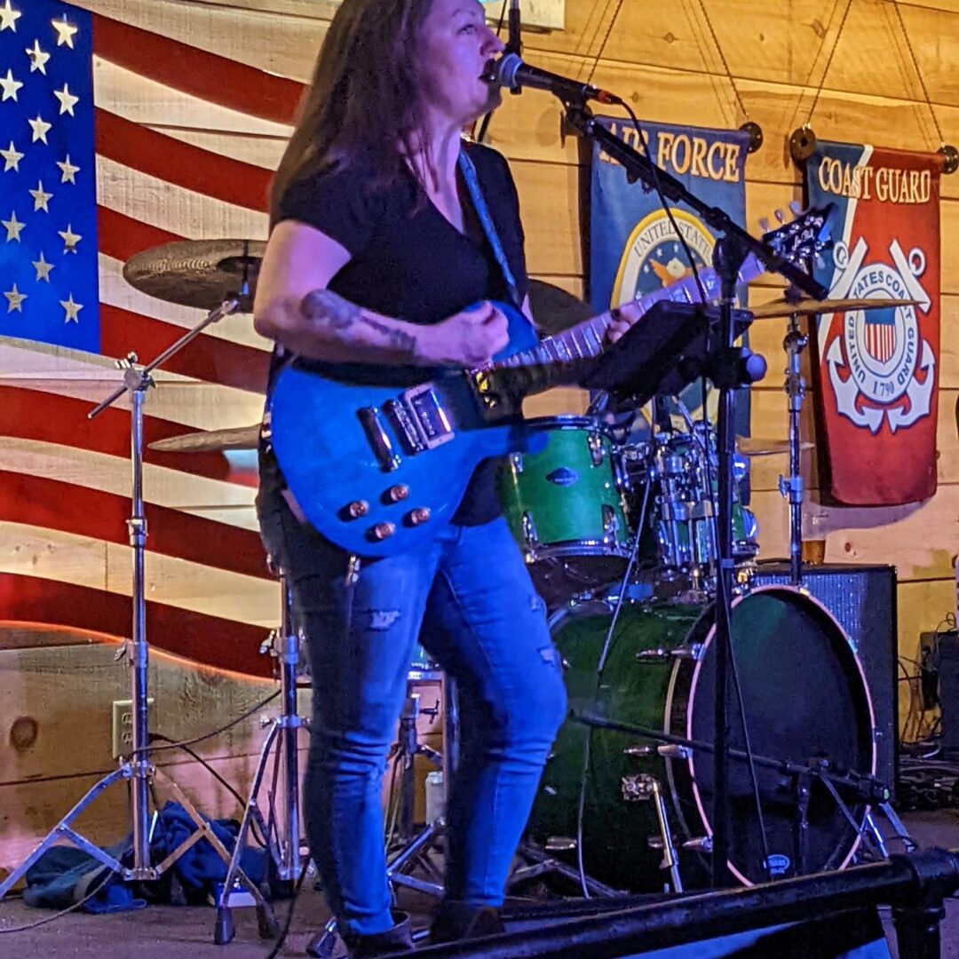 A woman playing guitar on stage with an american flag behind her.