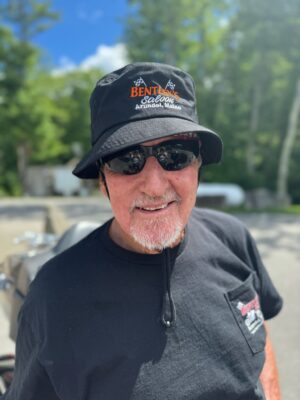 Smiling man wearing sunglasses and a bucket hat outdoors.